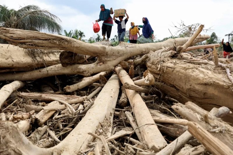 Indonesians navigate over logs to access flood relief center